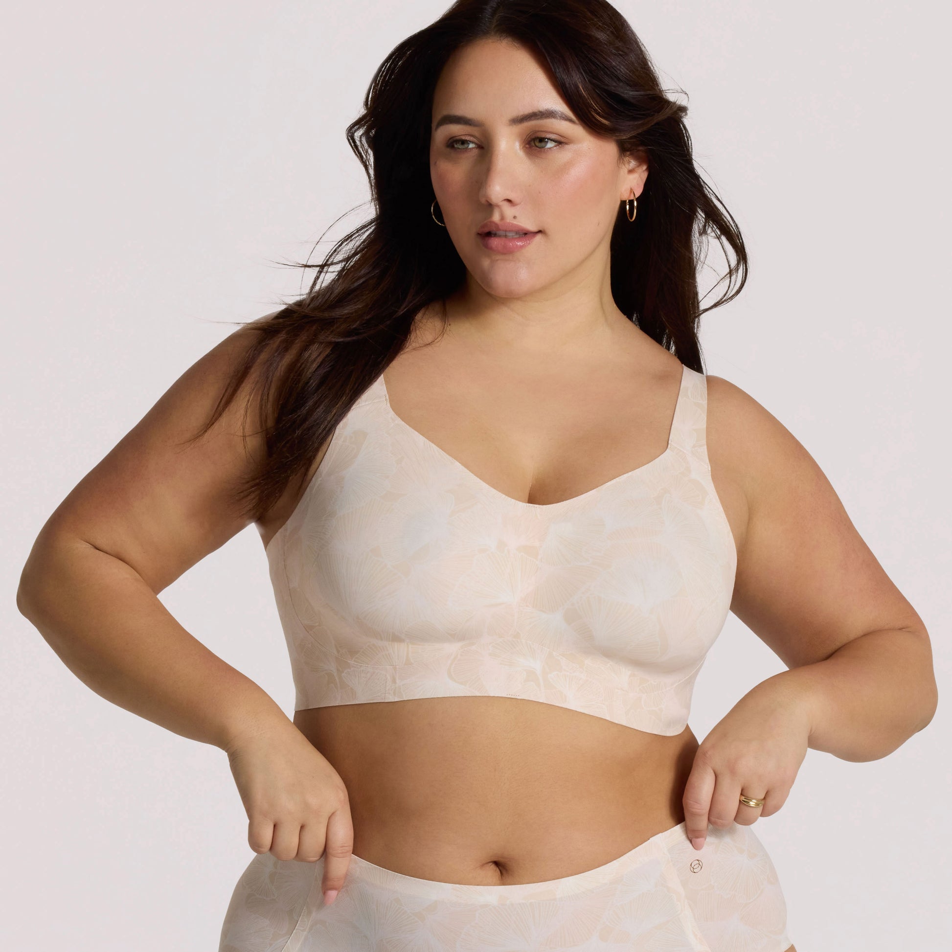 Woman wearing a beige patterned bralette against a plain background