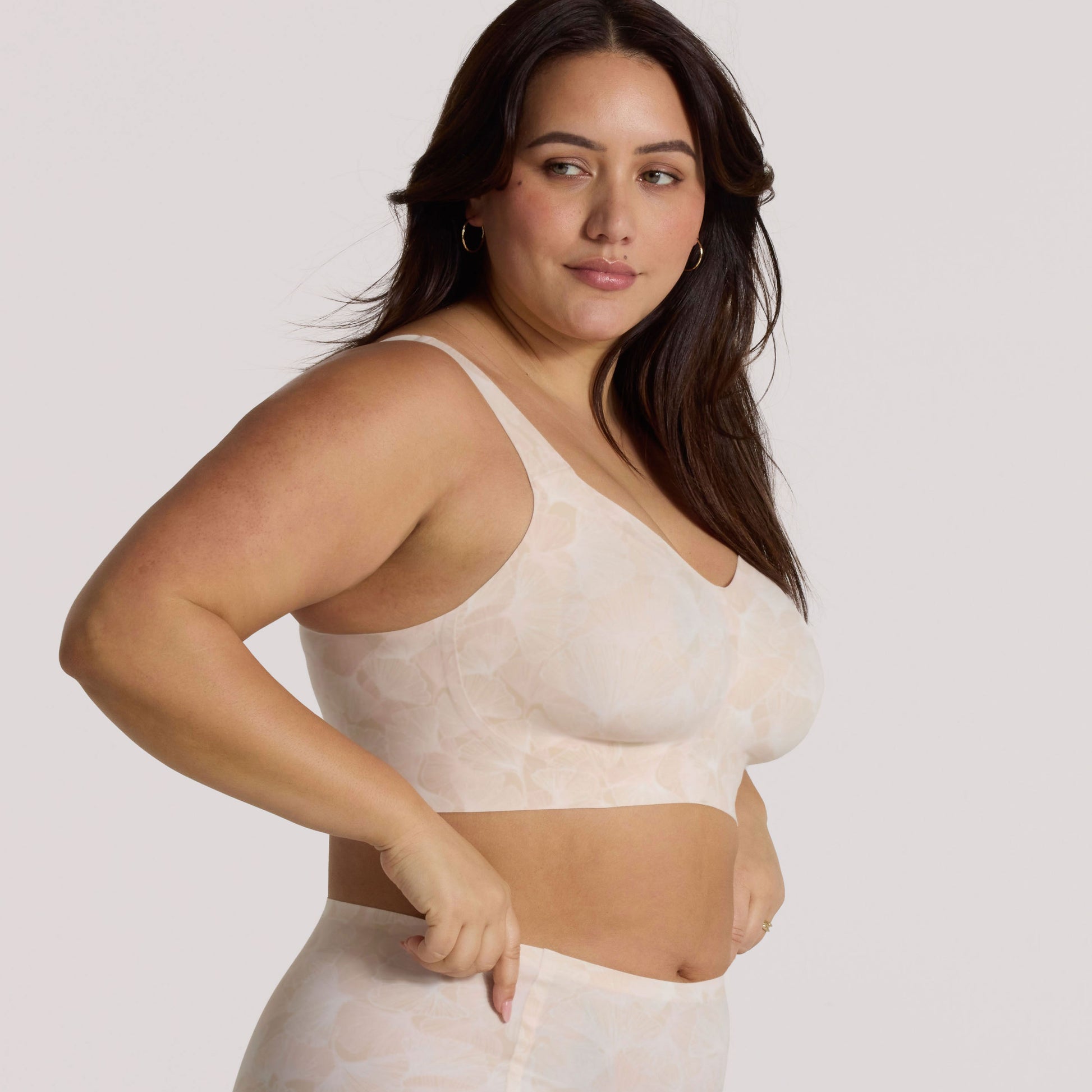 Woman wearing a beige bralette against a plain background