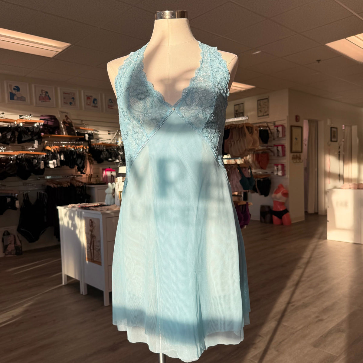 A light blue sleeveless lace and mesh dress displayed on a mannequin inside a clothing store.