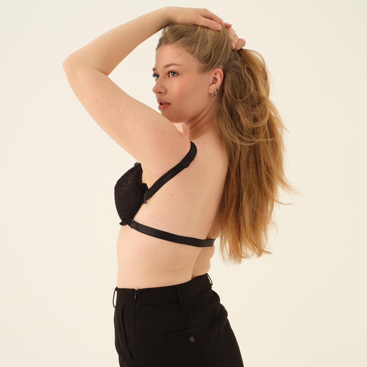 A woman posing from the back wearing a black lace and satin halter bralette and a black mini skirt against a plain off-white background.