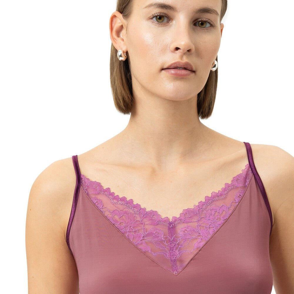 A woman wearing a mauve-colored camisole top with a purple lace V-neckline, photographed against a plain light gray studio background.