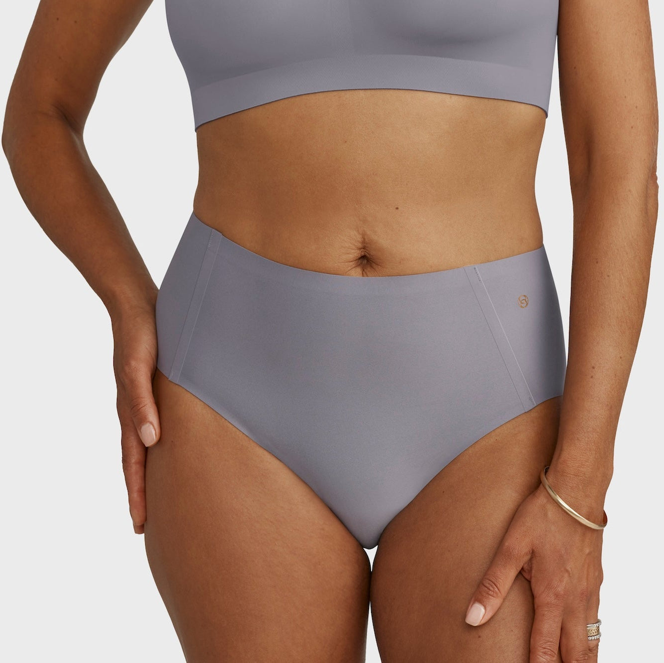 Person wearing a gray sports bra and high-waisted underwear on a plain background