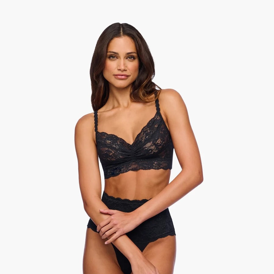 A woman modeling a black lace bralette and matching high-waisted briefs against a plain light gray studio background.