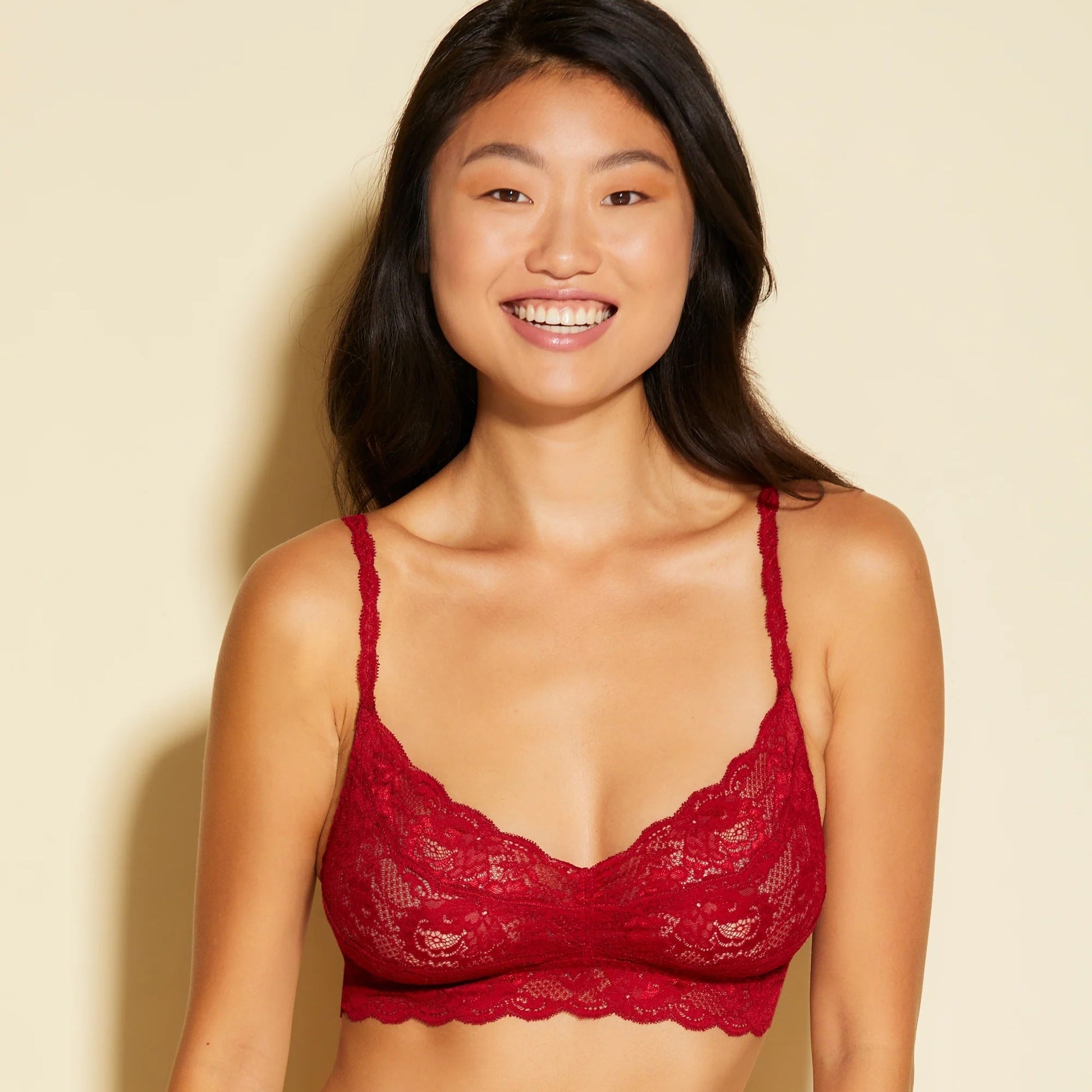 Woman wearing a red lace bralette against a beige background
