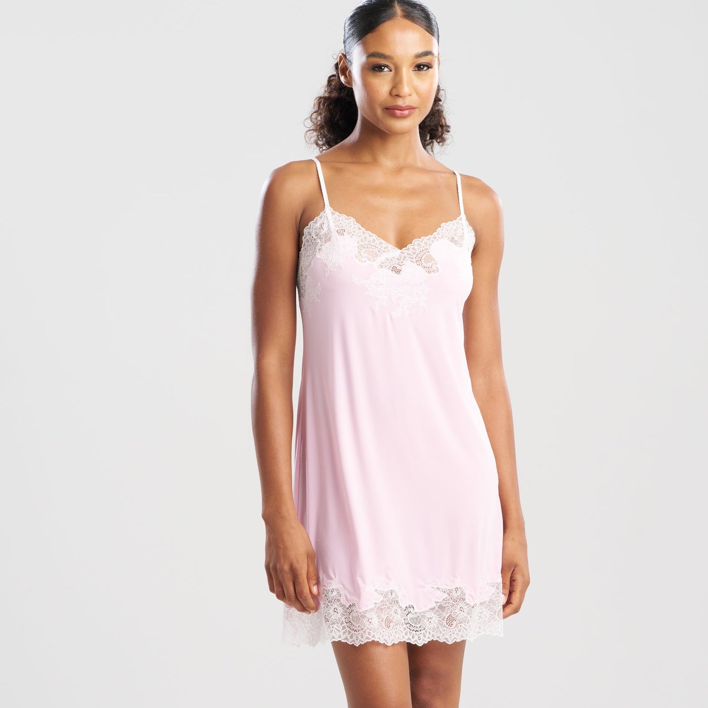 Woman wearing a light pink slip dress with lace details on a white background