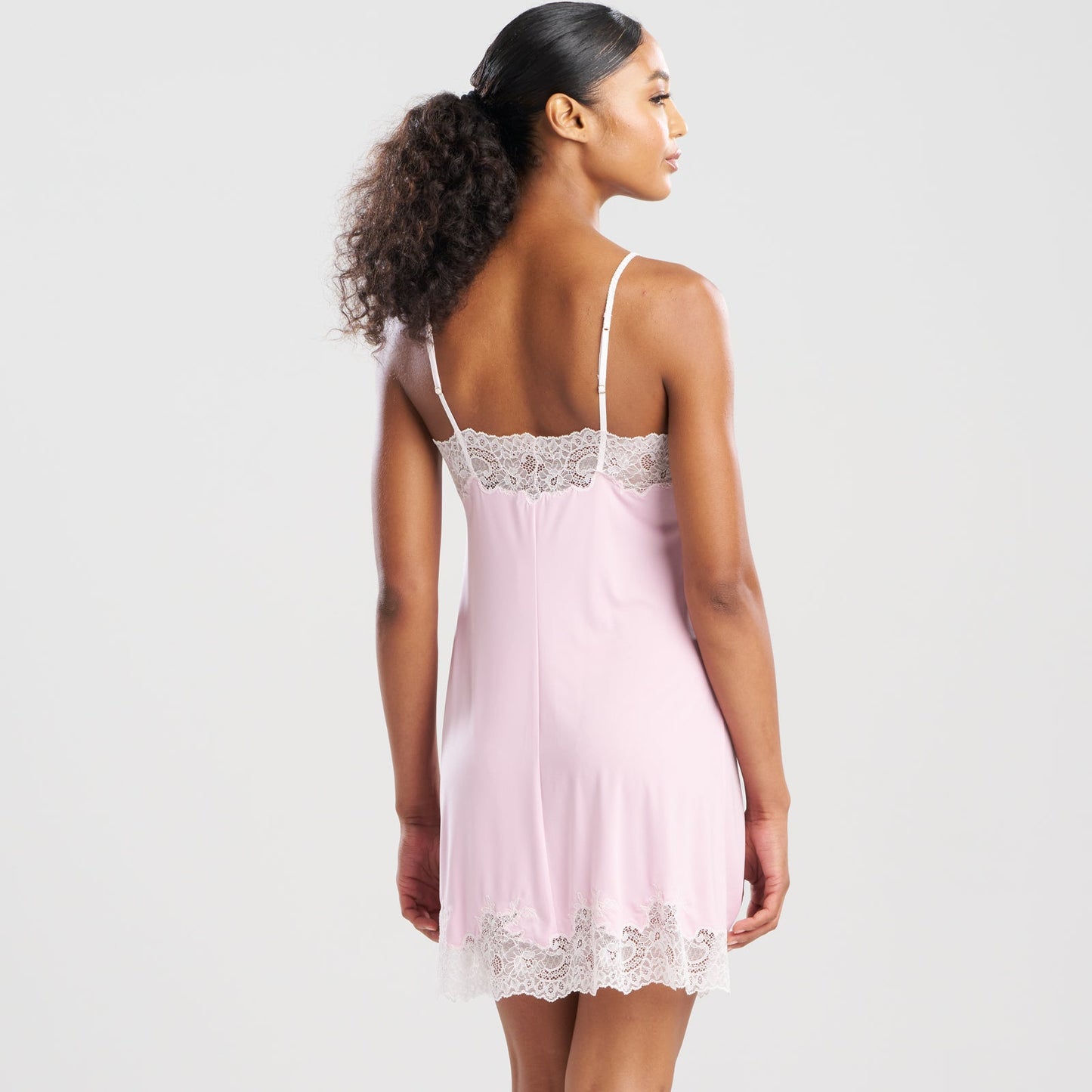 Woman wearing a pink slip dress with lace details on a white background