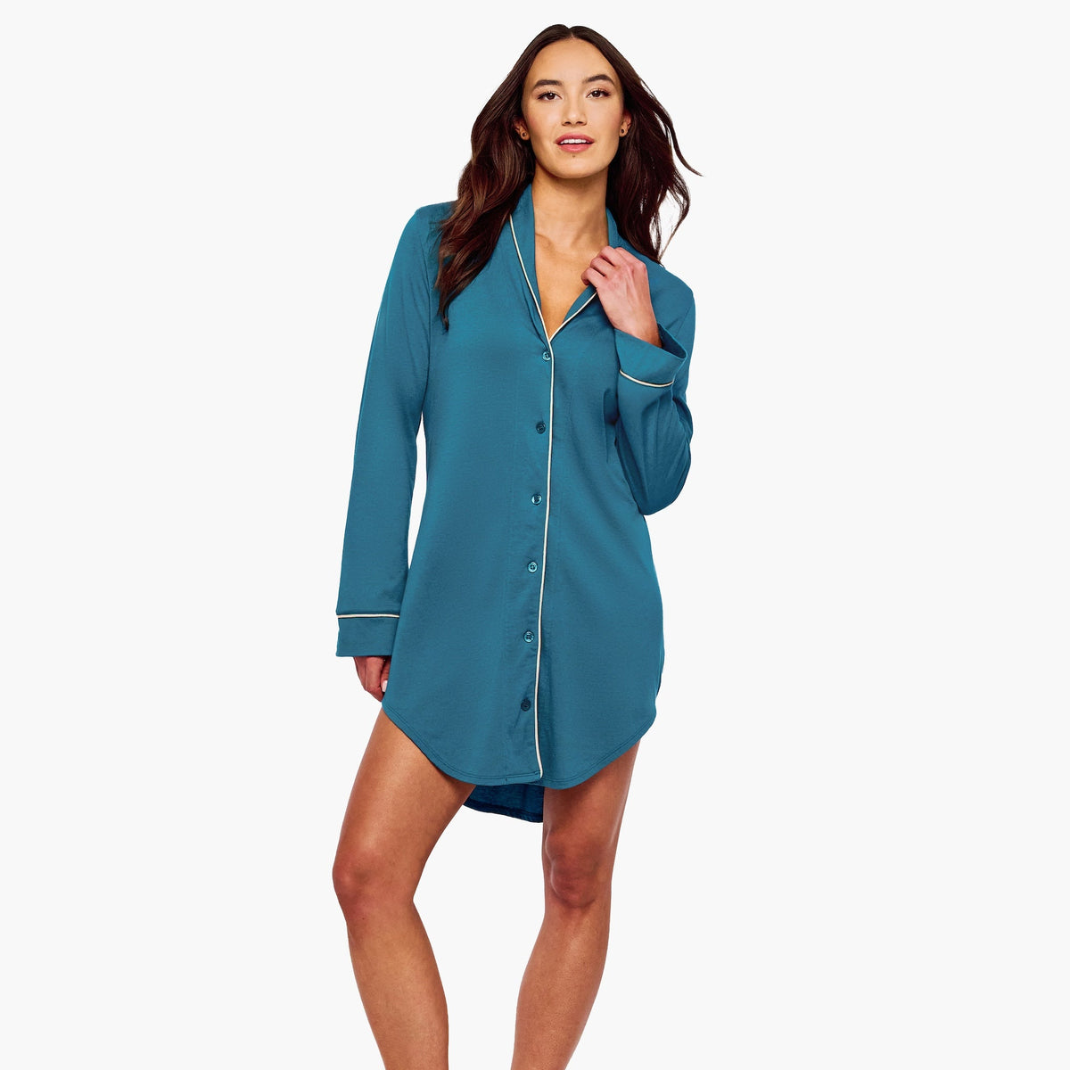 A woman modeling a teal blue long-sleeve pajama shirt dress with white piping details, standing against a plain white background.