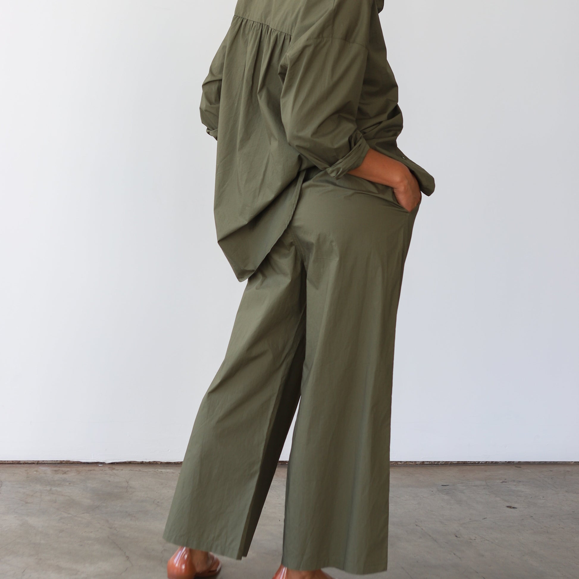 Person wearing an olive green outfit standing against a white wall.