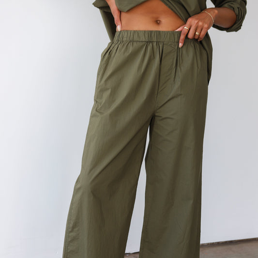 Person wearing olive green pants and a cropped top against a white wall.