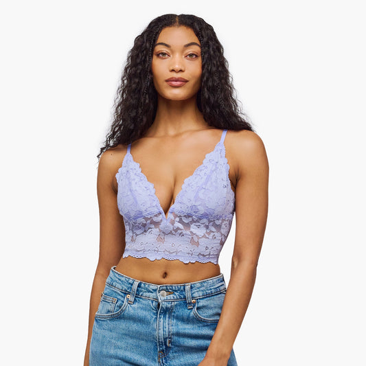 Woman wearing a light purple lace bralette and blue jeans on a white background
