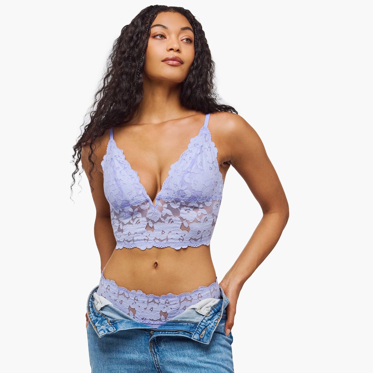 Woman wearing a light blue lace bralette and underwear set with jeans on a white background