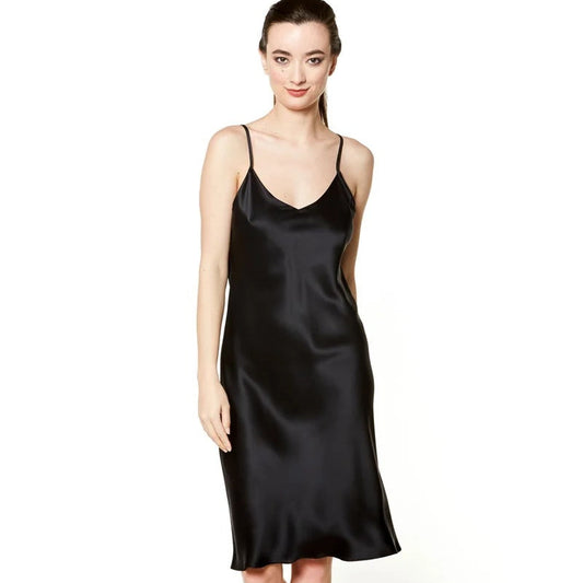 A woman modeling a black satin slip dress with thin spaghetti straps and a V-neckline, paired with black strappy high-heeled sandals, against a plain white studio background.