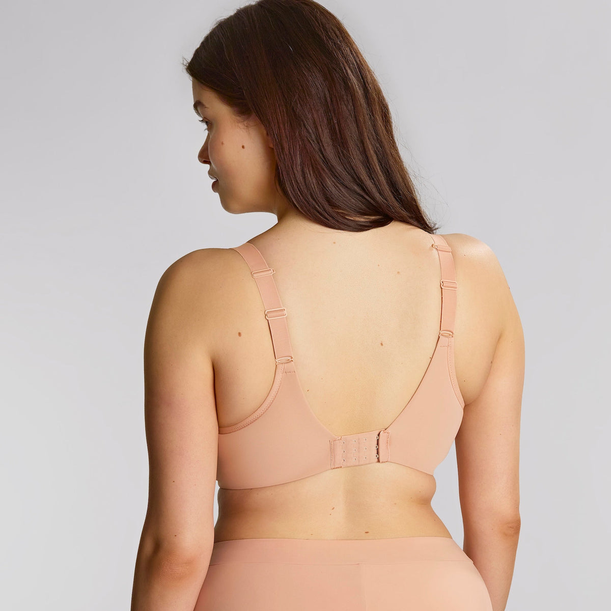 Woman wearing a beige bodysuit against a plain background
