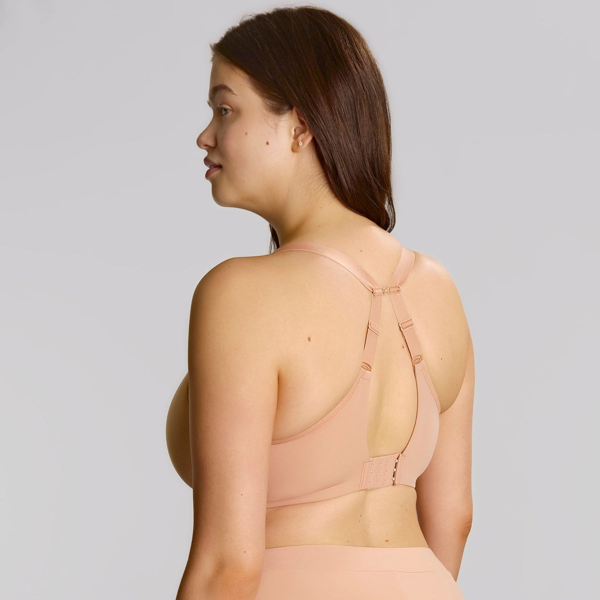 A woman shown from the back wearing a nude-beige seamless bra and matching high-waisted briefs against a solid light gray studio background.