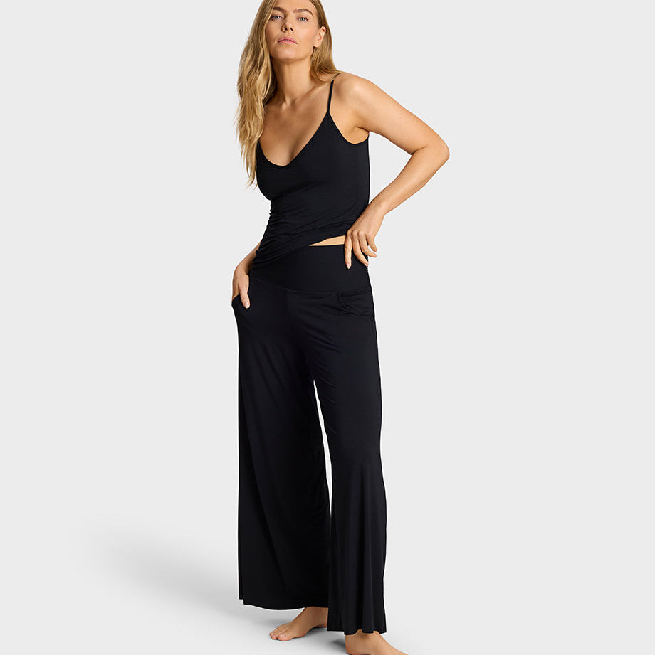 A woman modeling a black sleeveless camisole top and matching wide-leg pants set against a light gray studio background.