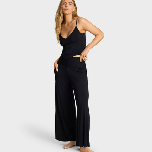 A woman modeling a black sleeveless camisole top and matching wide-leg pants set against a light gray studio background.