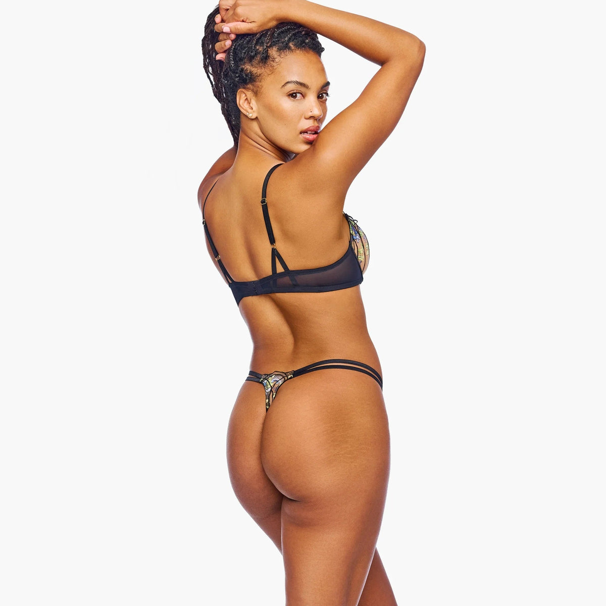 A woman posing from the back wearing a black mesh bikini with patterned trim, set against a solid white background.