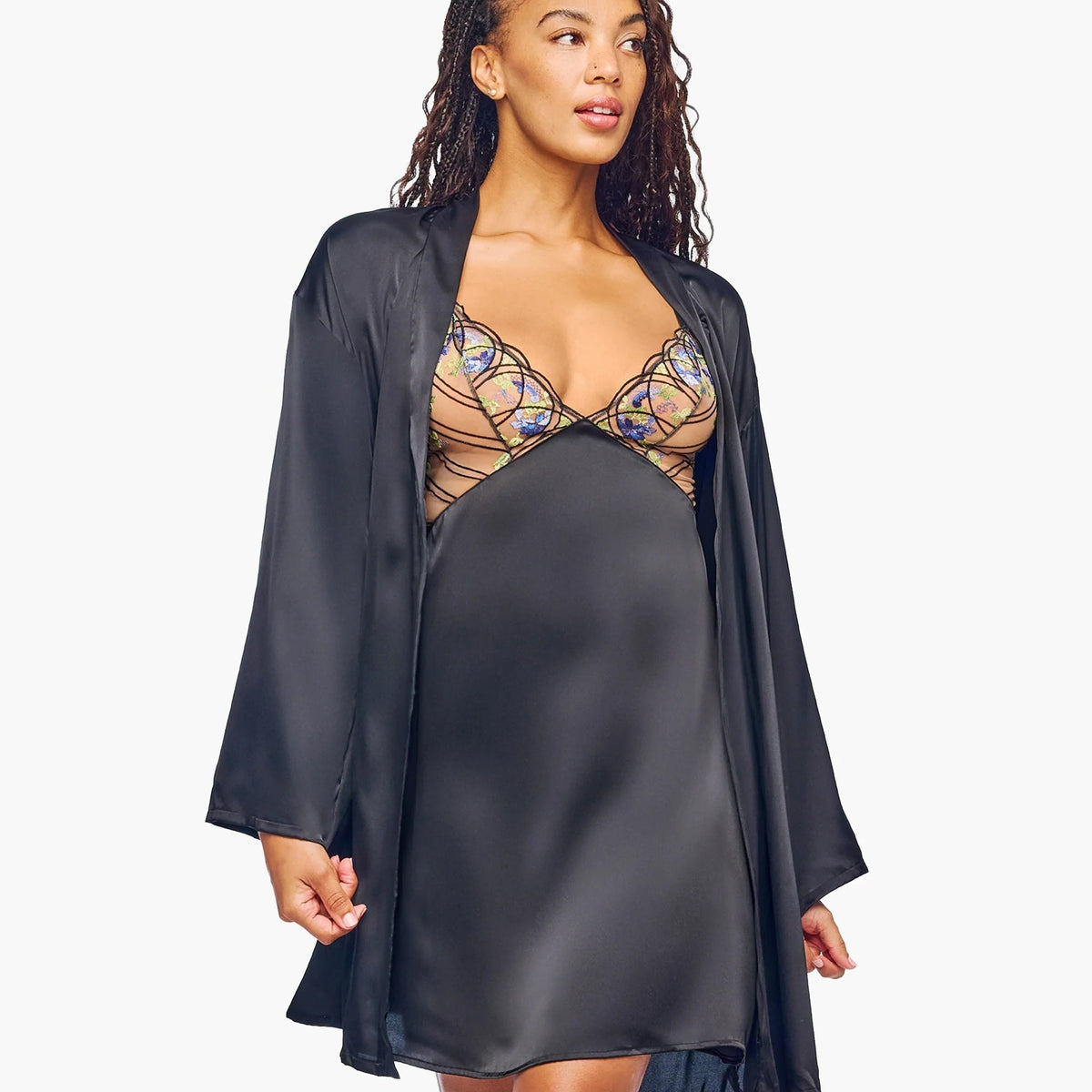 A model wearing a black satin slip dress and a matching black satin robe over a beige lace maternity bra, photographed against a solid white background.