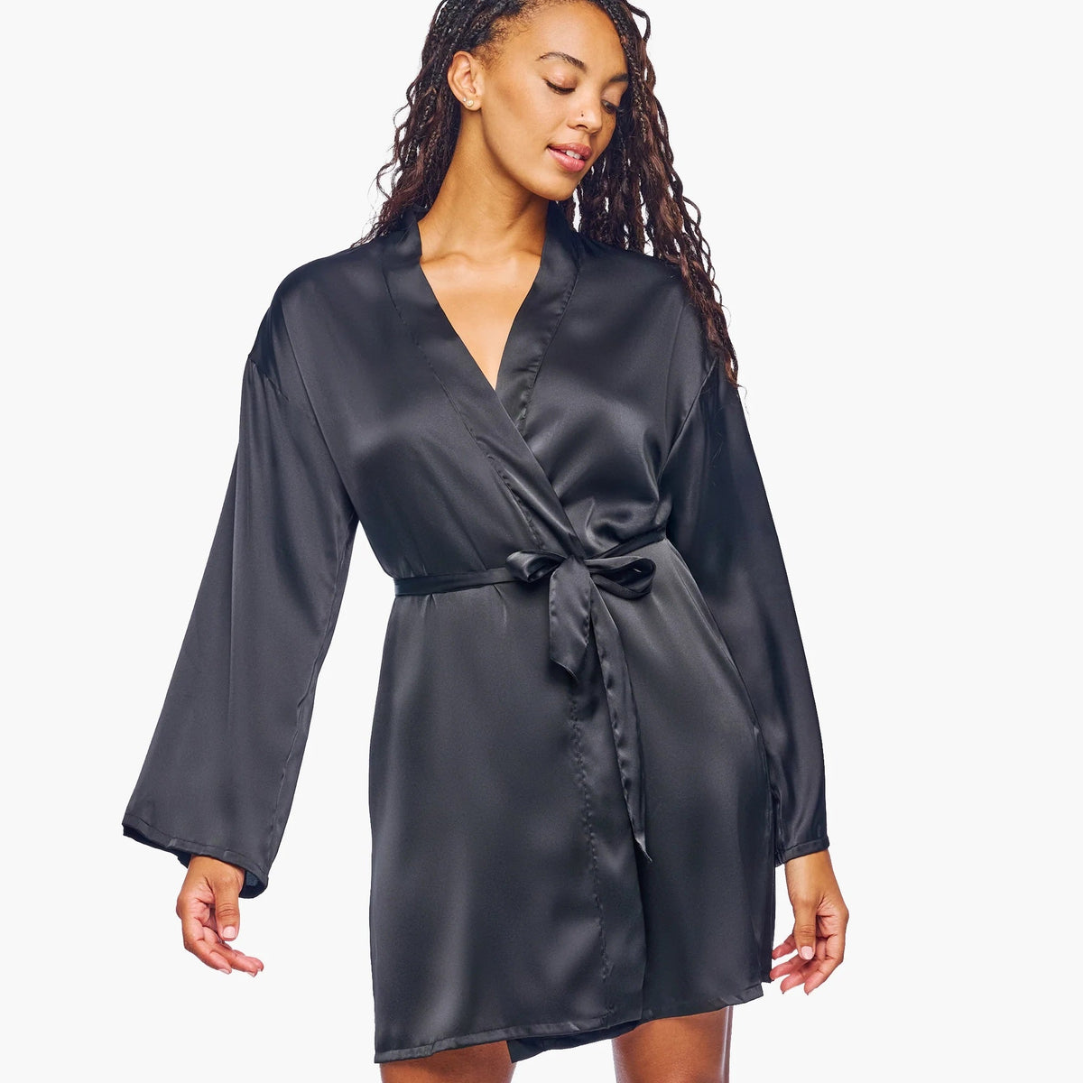 A woman modeling a black satin wrap robe with a tie waist, shown against a plain light gray studio background.