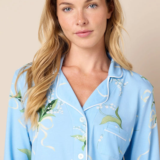 A woman wearing a light blue pajama shirt with a green and white botanical print, photographed against a solid beige background.