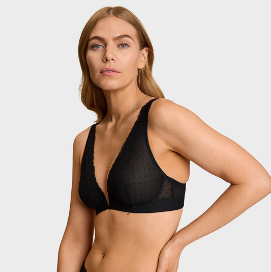 A woman modeling black sheer mesh and lace lingerie, featuring a V-neck bralette and matching high-waisted briefs, against a light gray studio background.